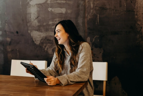 Woman using a tablet while sitting at a wooden table.